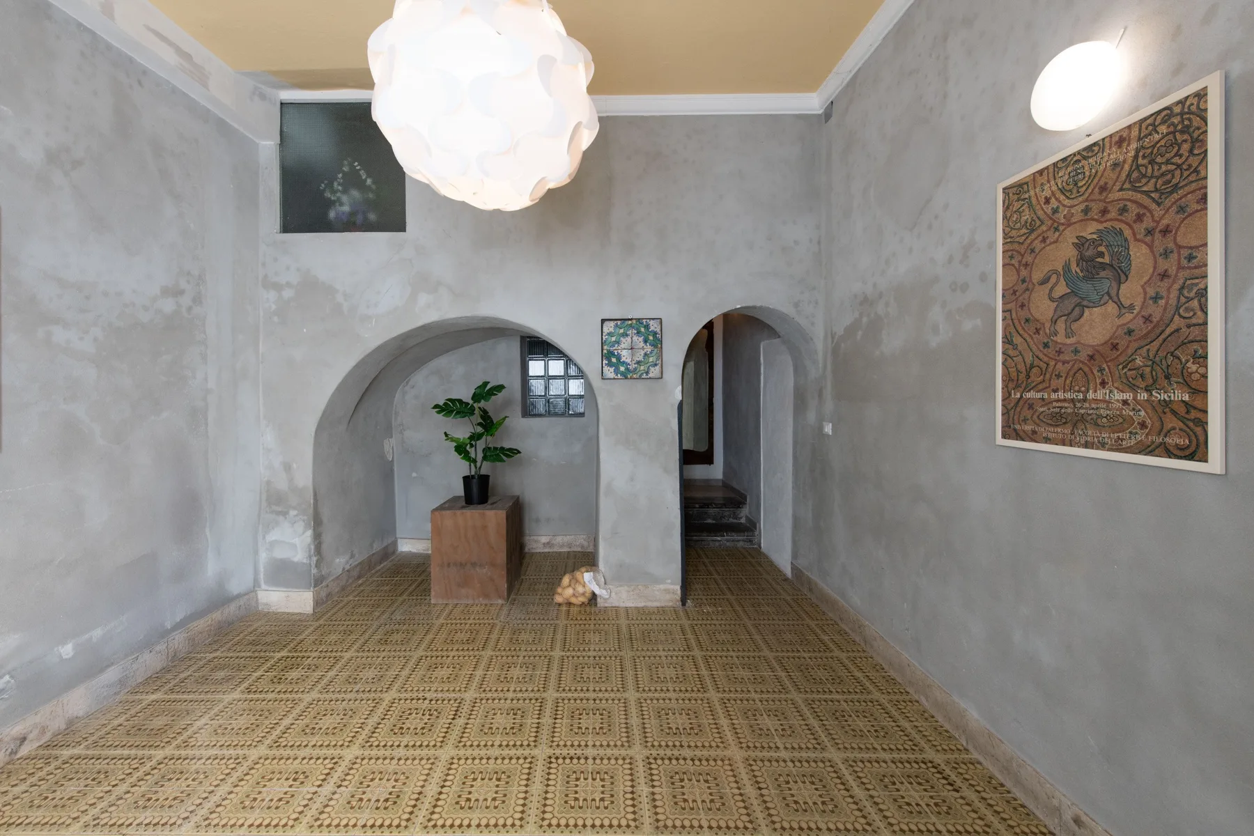 A gray-walled room with arched openings, patterned flooring, and a potted plant.