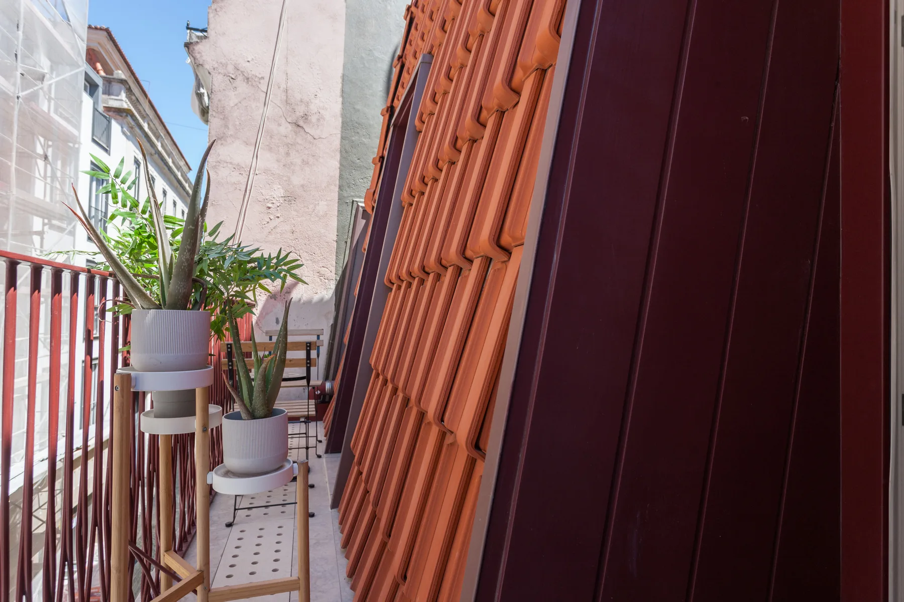 A narrow balcony with potted plants and a small seating area.