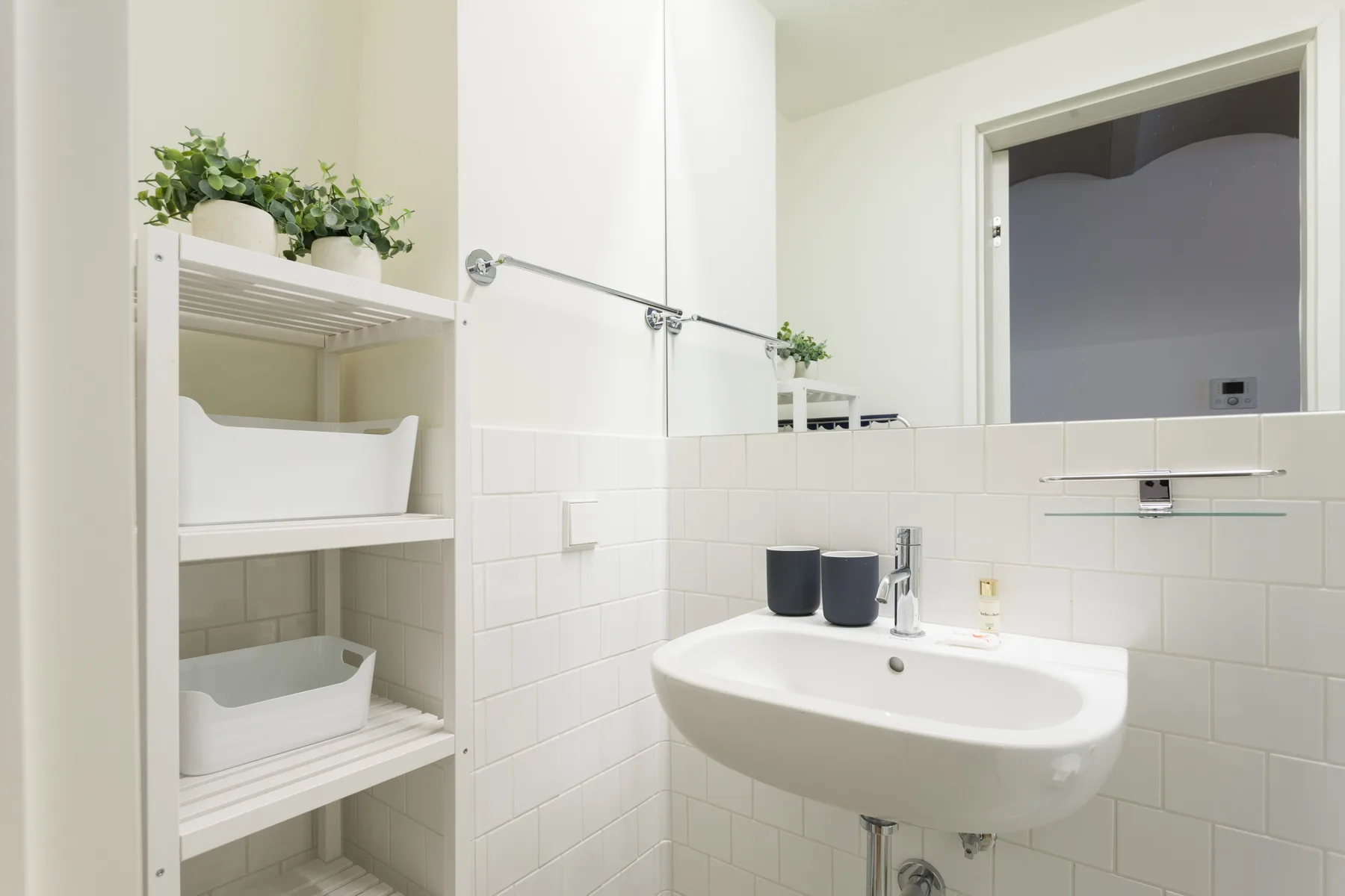 A bright bathroom with a wall-mounted sink and open shelving.