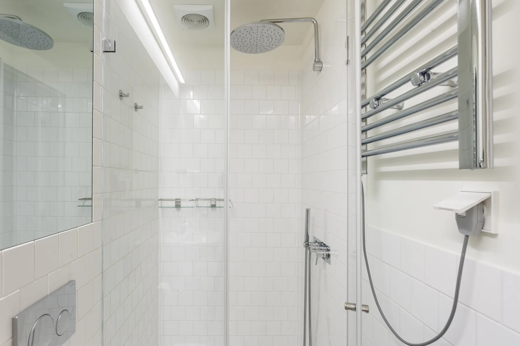 A tiled bathroom with a wall-mounted shower and towel warmer.