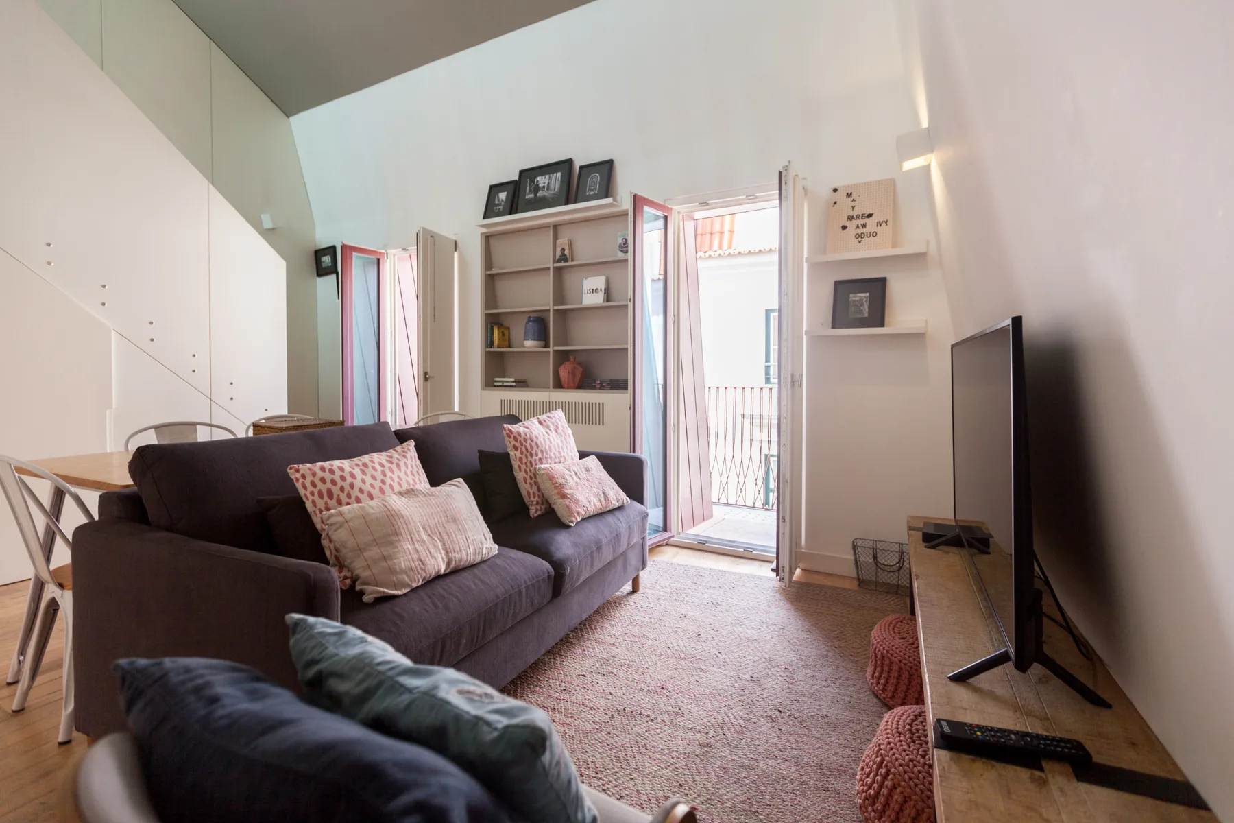 A bright living room with a sofa, television, and doors opening to a balcony.