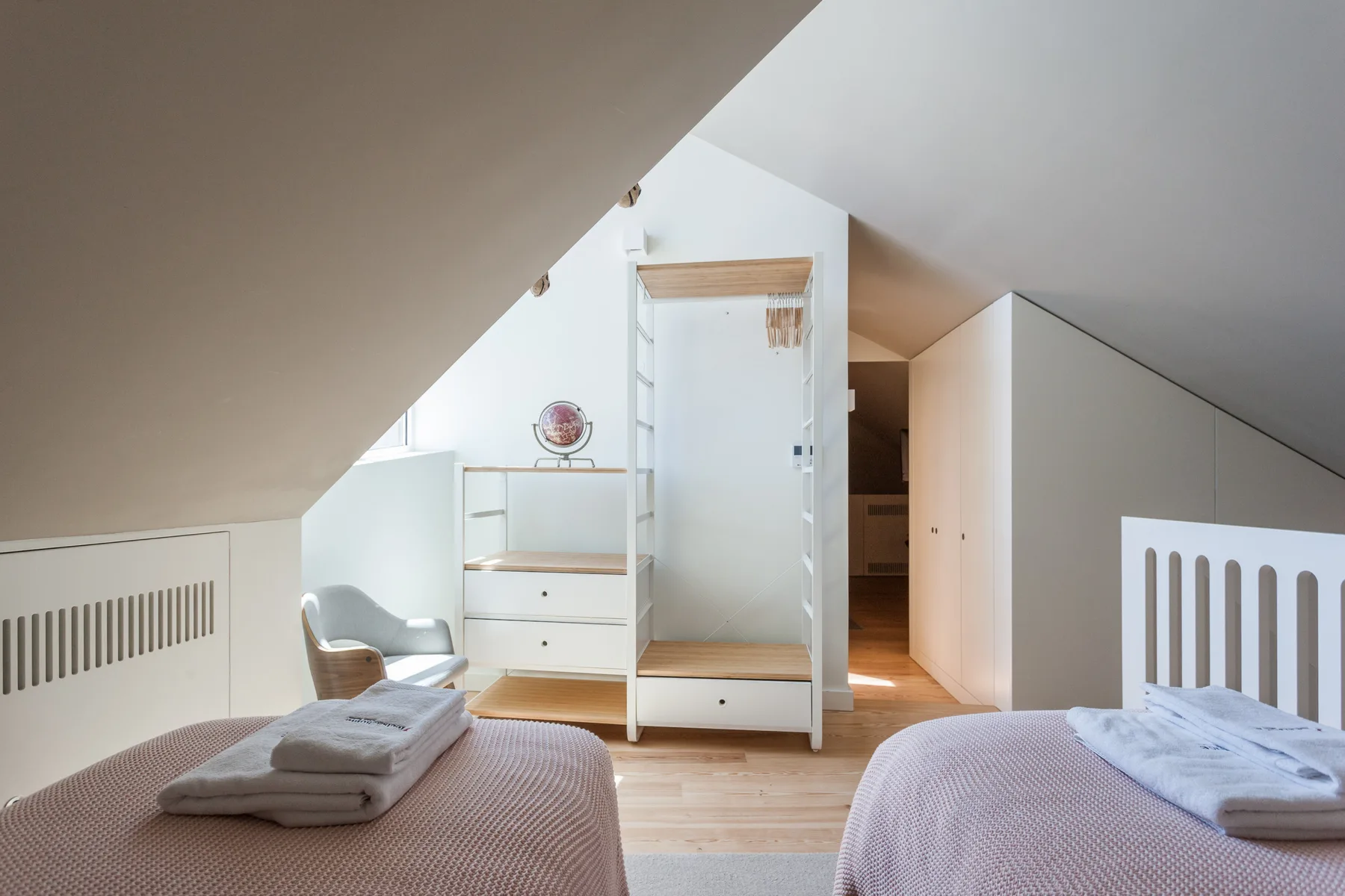 An attic bedroom with two beds and a light wood floor.