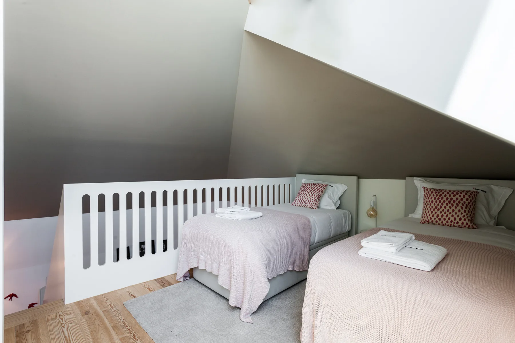A bedroom with two beds, folded towels, and a white railing.