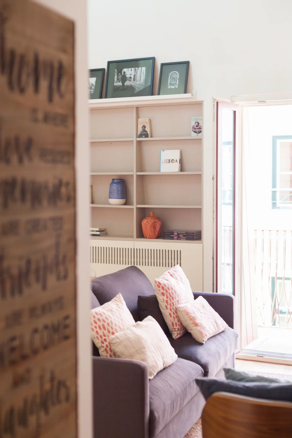 Living room with seating, decorative pillows, and a shelf beside an open balcony door.