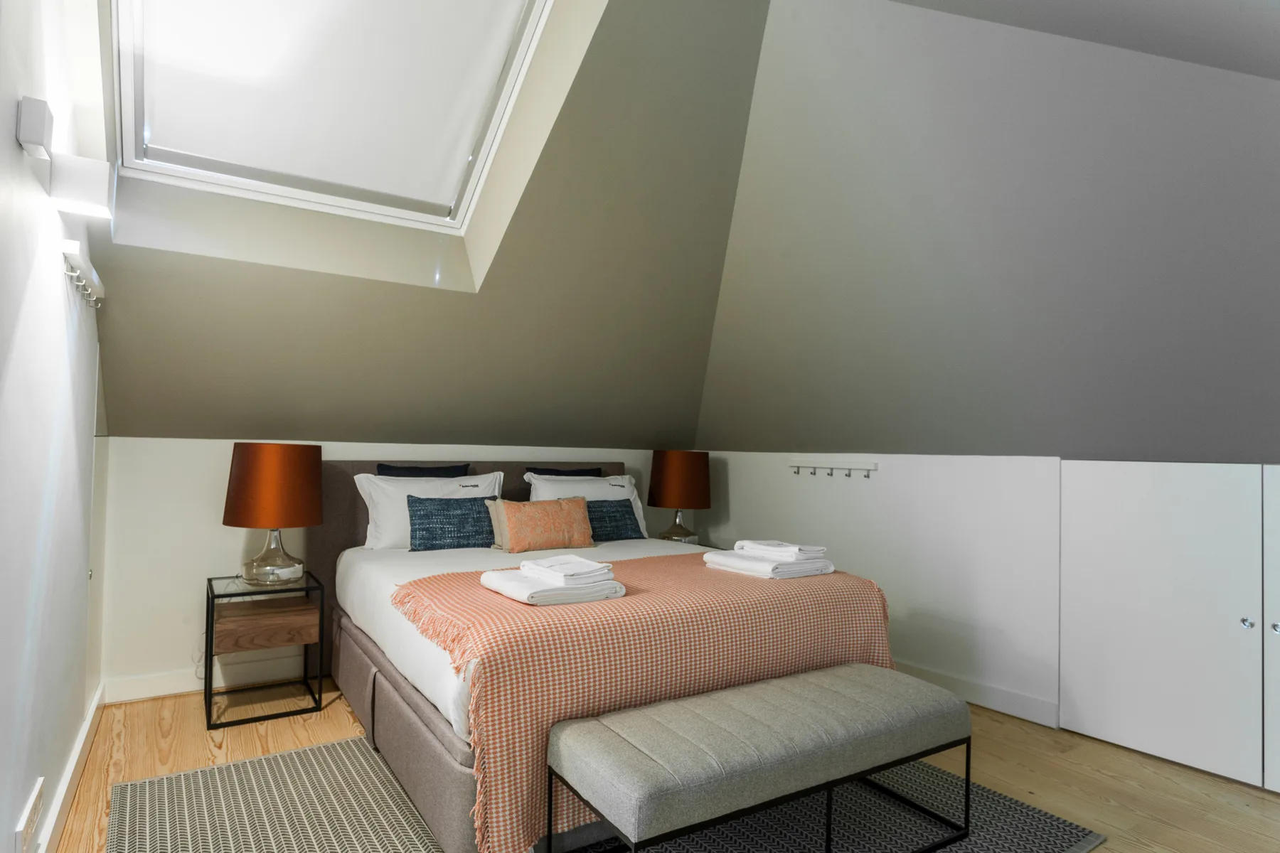 A bedroom with a double bed, folded towels, and a bench at the foot.
