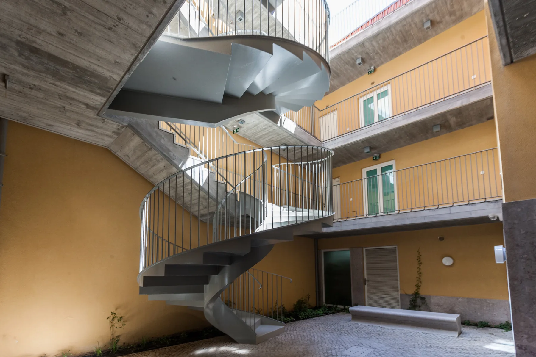 An open courtyard with a curved staircase and balconies along the walls.