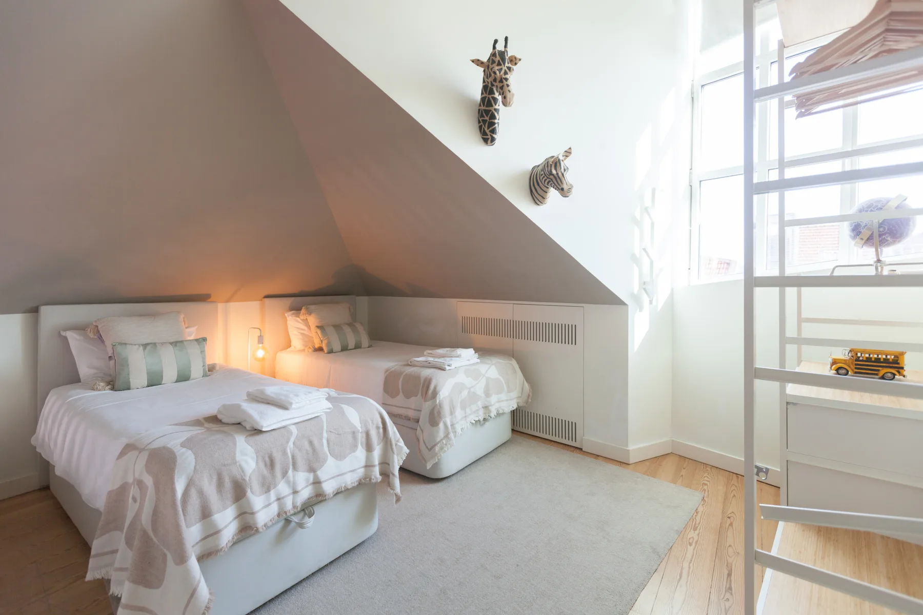 A bright bedroom with two beds beneath a sloped ceiling and a large window.