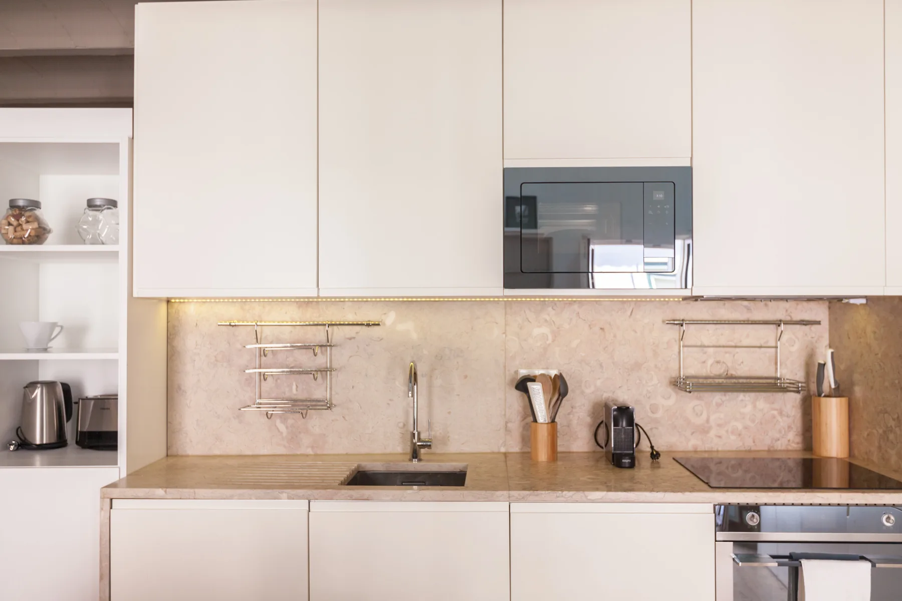A modern kitchen with white cabinets, a cooktop, and an oven.