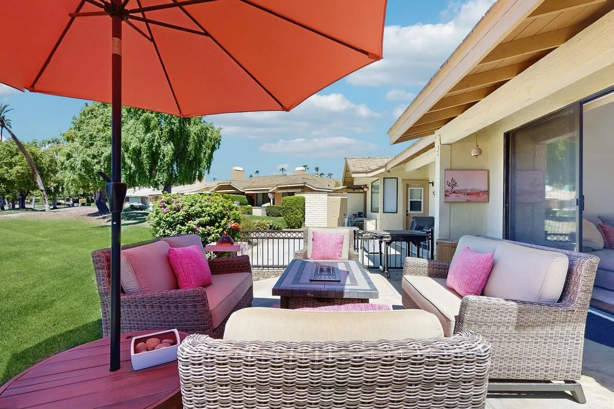 An outdoor patio with wicker seating, a low table, and a large umbrella.