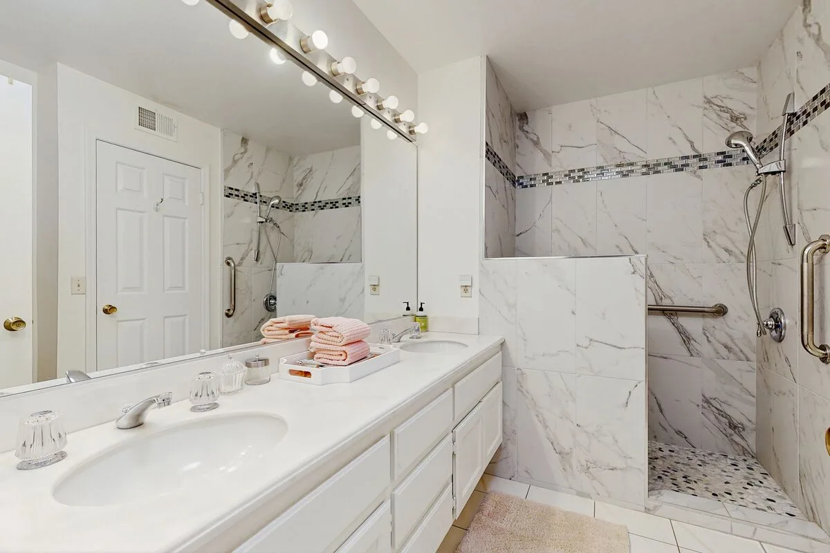 A bright bathroom with a long vanity and a walk-in shower.
