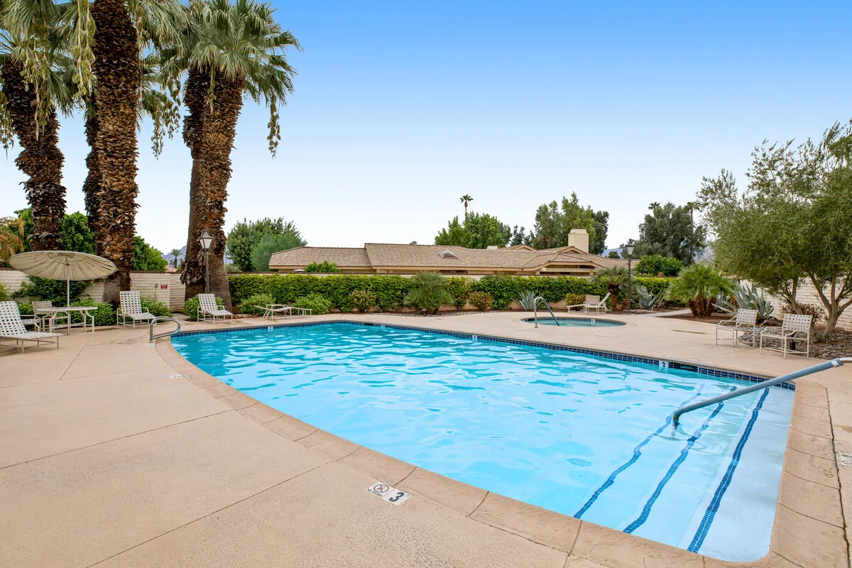 An outdoor swimming pool surrounded by palm trees and seating.