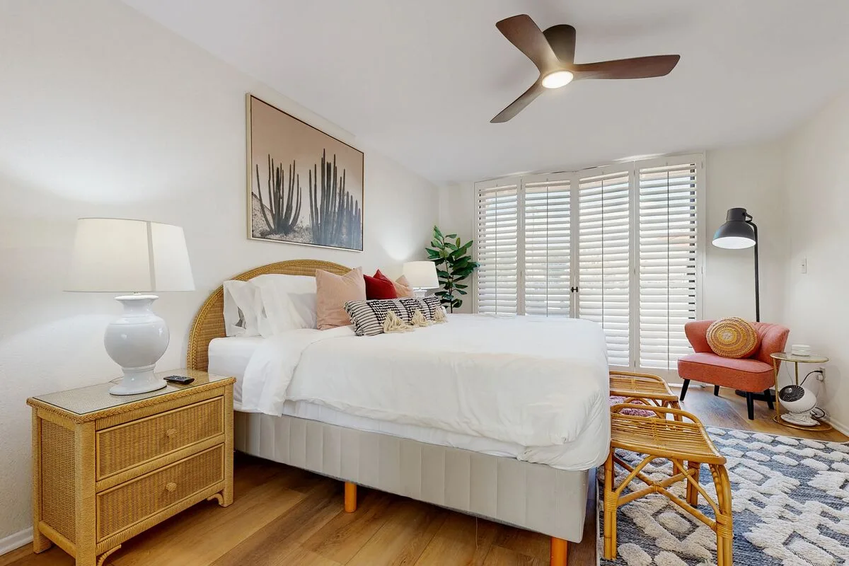 A bright bedroom with a bed, bedside table, and large shuttered windows.