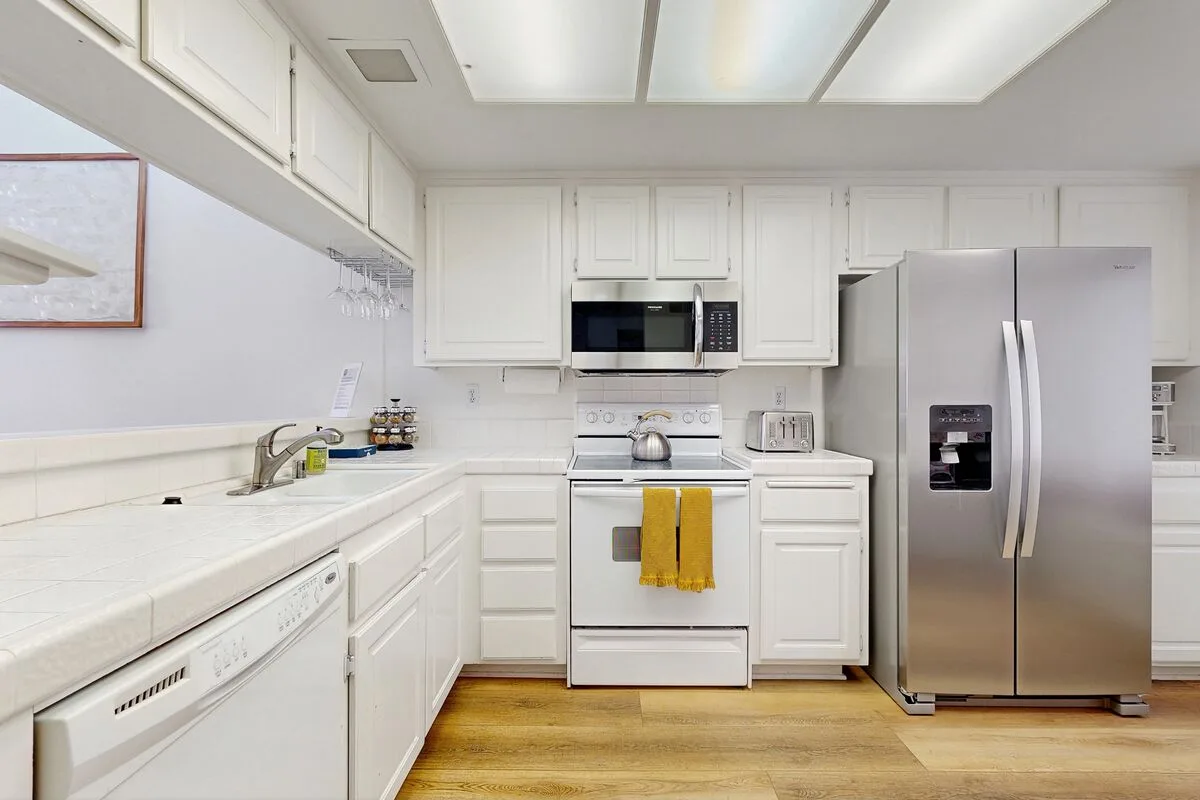 A bright kitchen with white cabinetry, a stove, and a stainless-steel refrigerator.