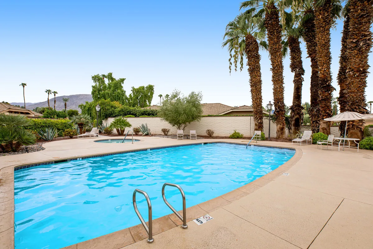 An outdoor swimming pool is surrounded by a paved deck and palm trees.