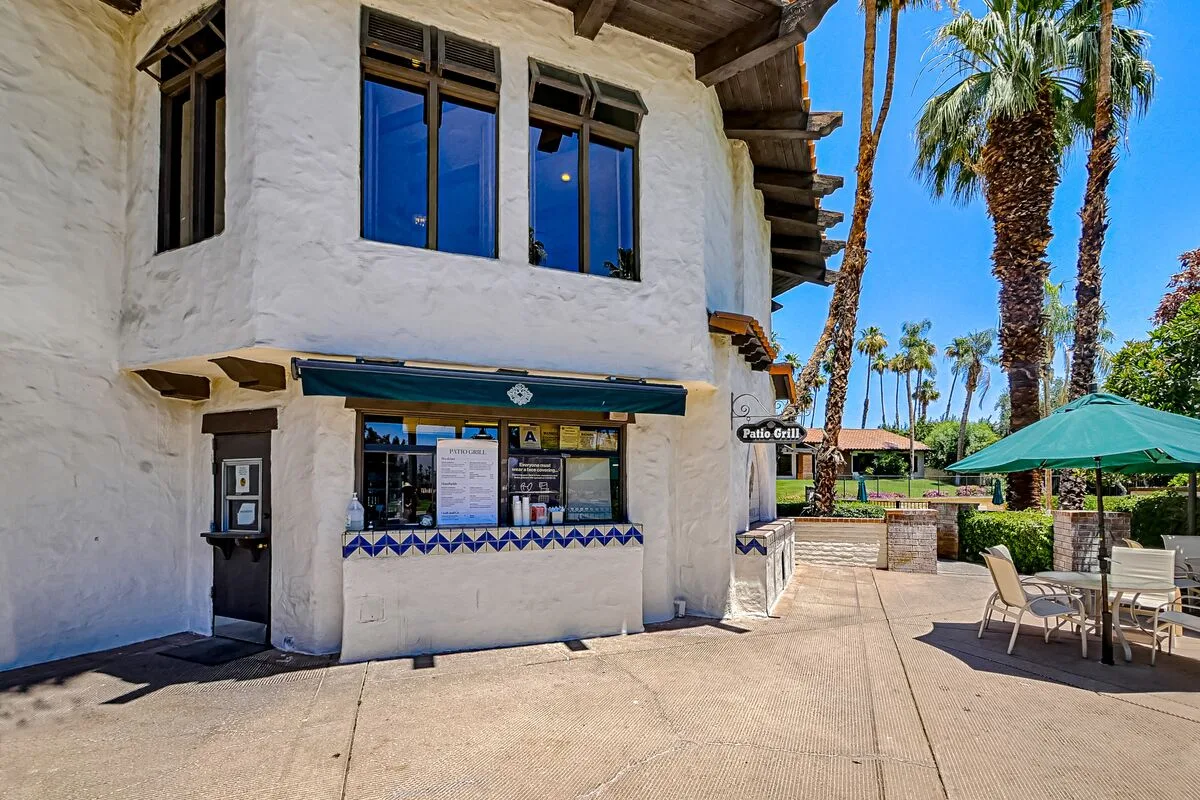 A small restaurant storefront opens onto a sunny patio with outdoor seating.