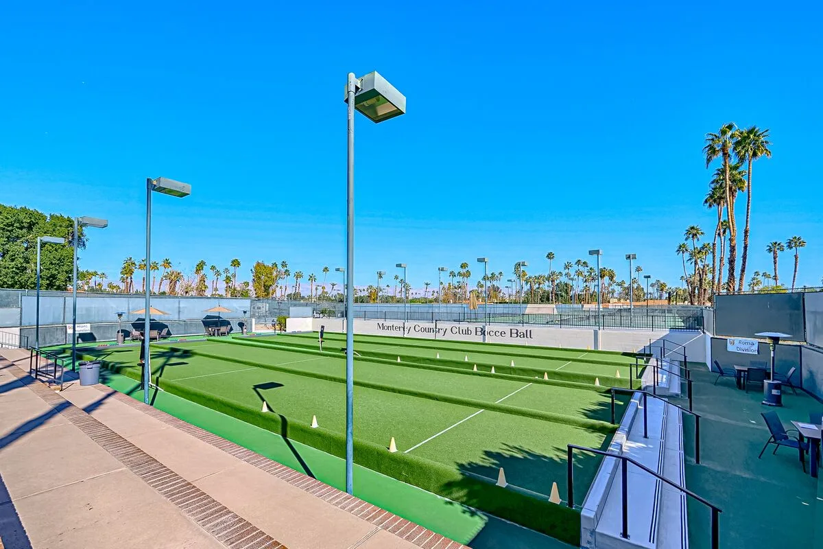 Outdoor court with green playing surface and surrounding fencing under a clear blue sky.