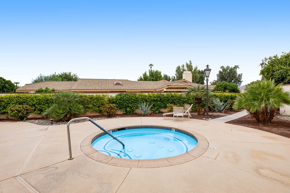 A small outdoor pool sits in a paved patio bordered by hedges and palms.