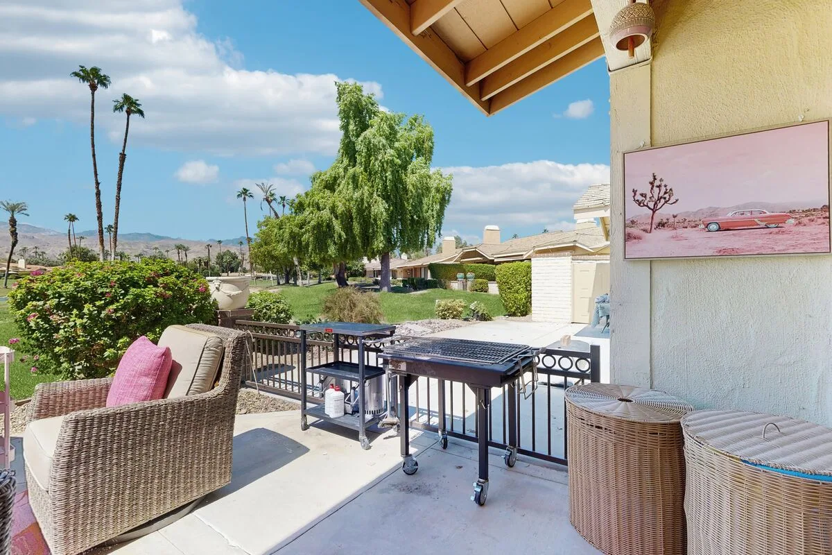 A patio seating area with wicker furniture and a table overlooks landscaped grounds.