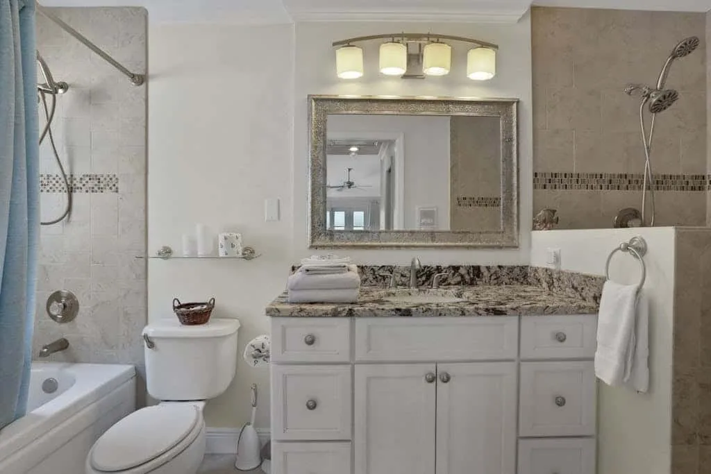 A bathroom with a bathtub, toilet, and vanity beneath a large mirror.