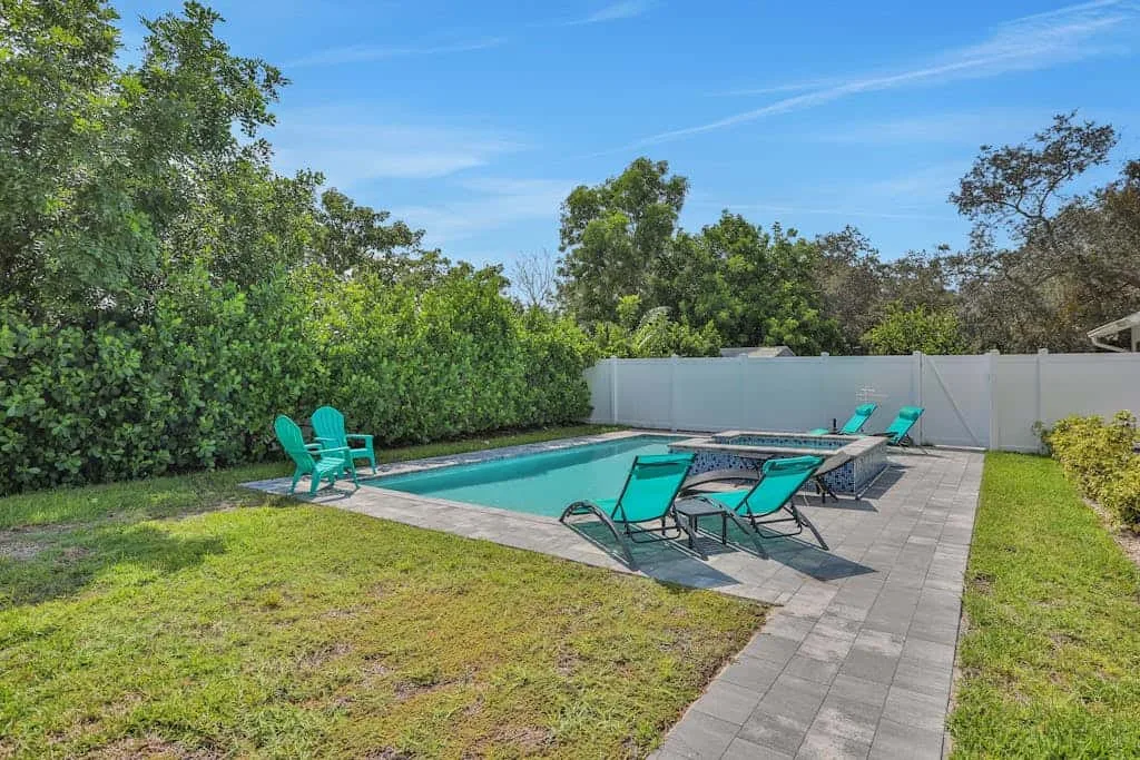 An outdoor swimming pool is surrounded by patio seating and greenery.