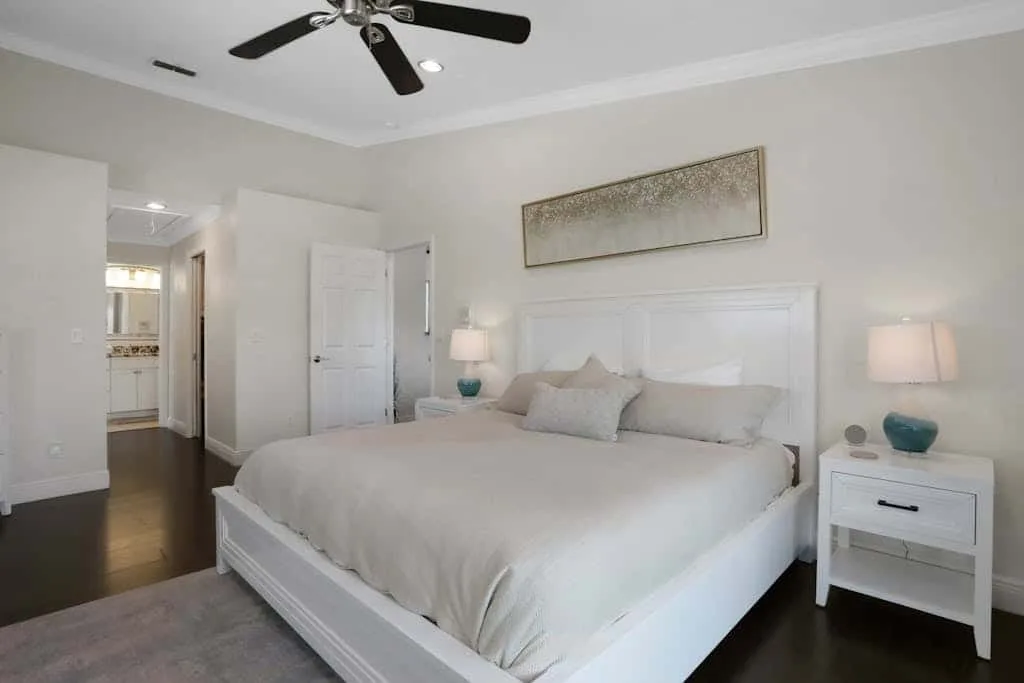 A bright bedroom with a large bed, bedside tables, and a ceiling fan.