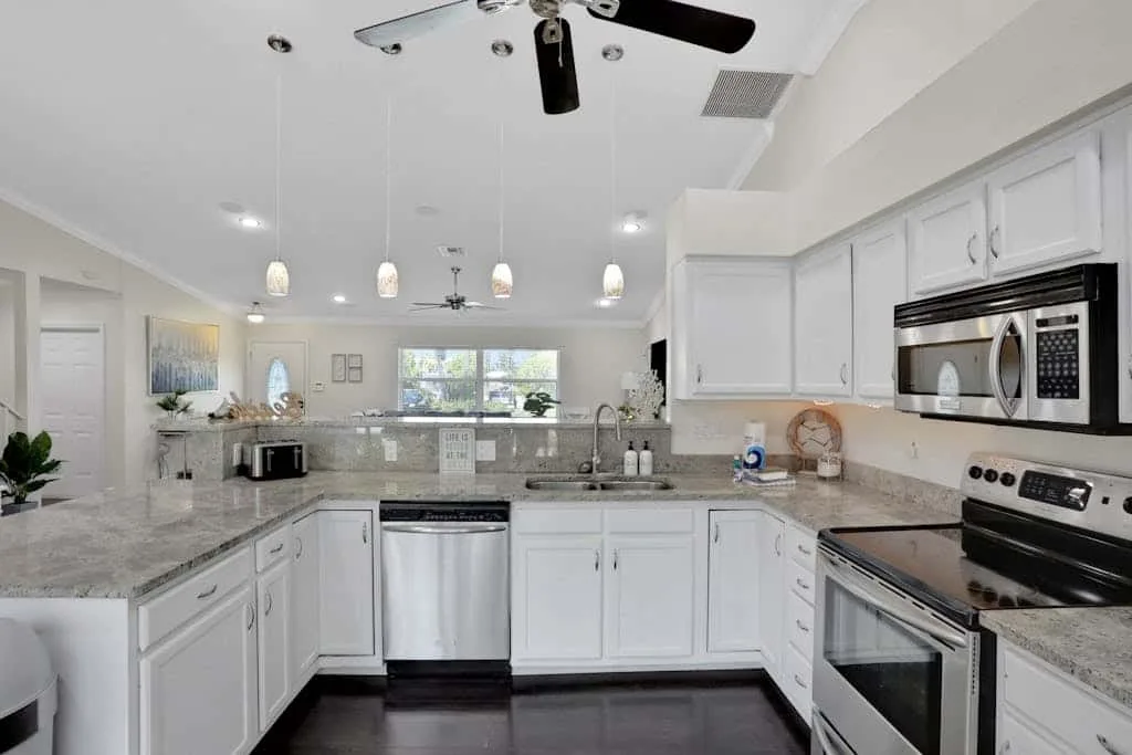 A bright kitchen with white cabinets, stone countertops, and stainless steel appliances.