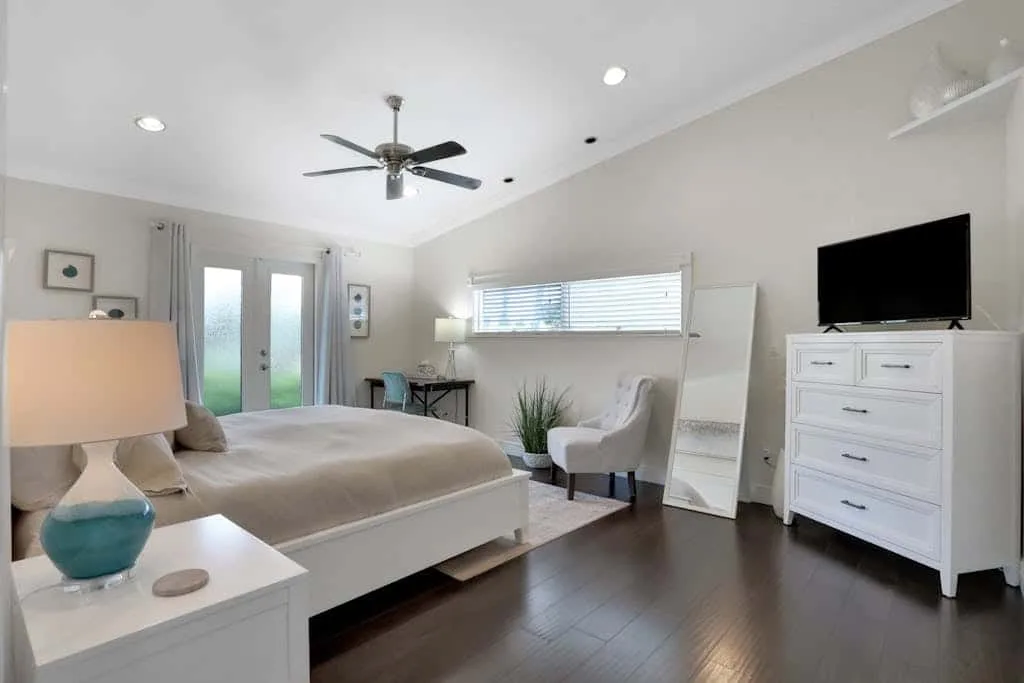 A bright bedroom with a bed, seating, and a television on a dresser.