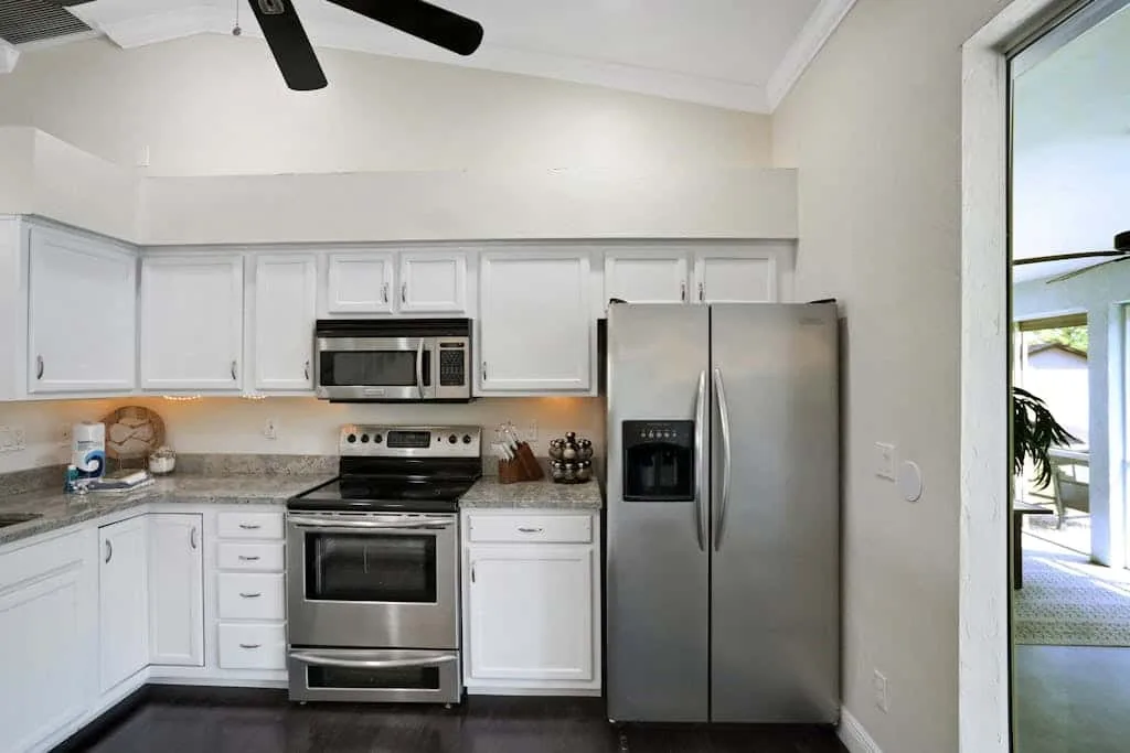 A bright kitchen with white cabinets, stainless steel appliances, and a ceiling fan.