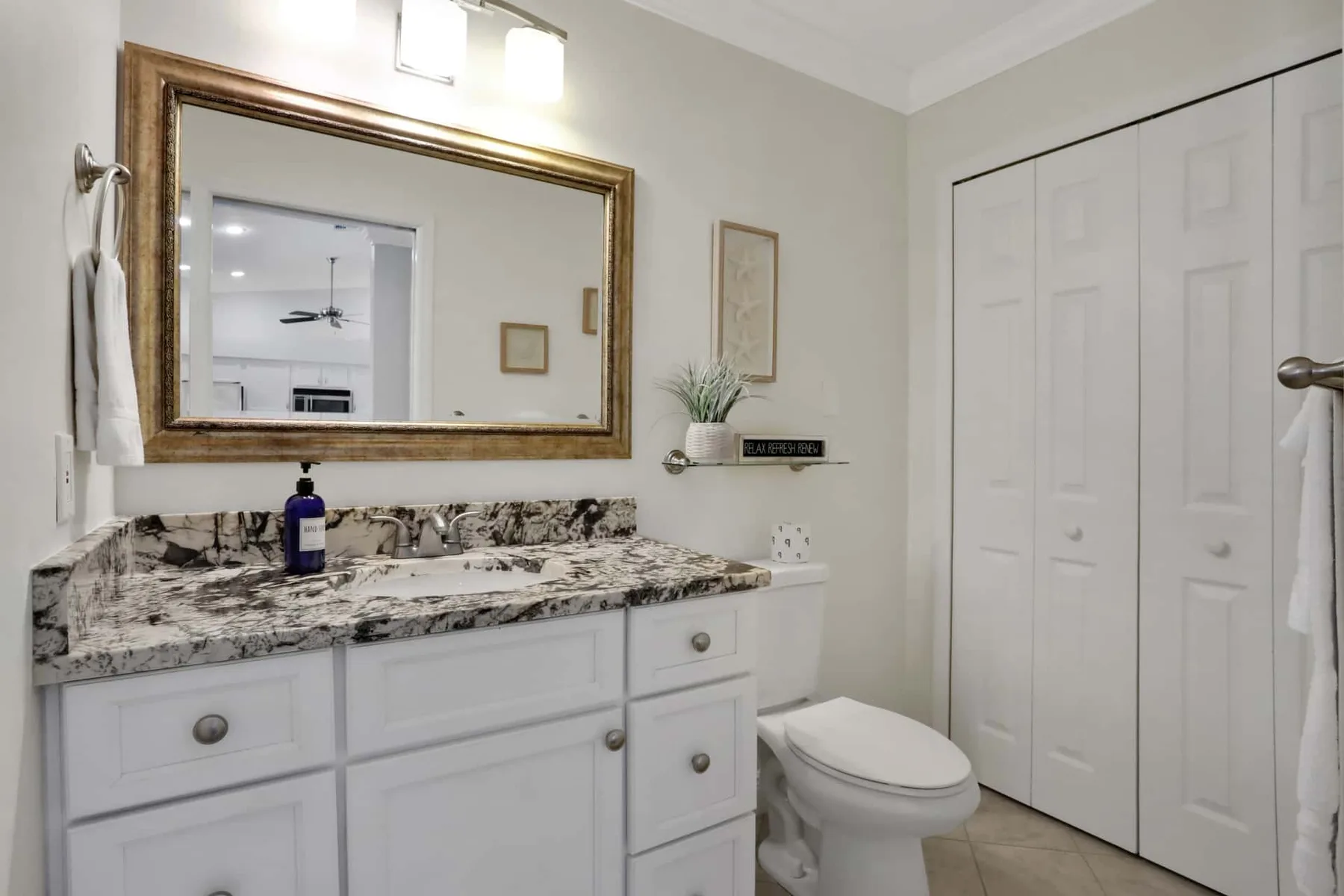 A bathroom vanity with a large mirror, countertop, and toilet.