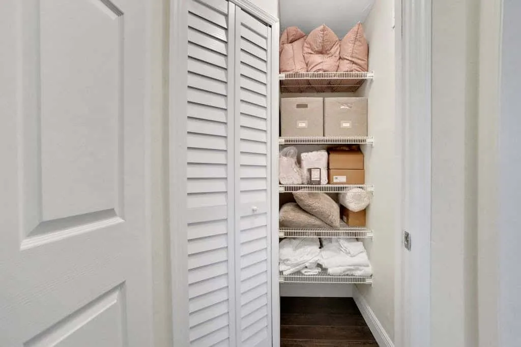 A narrow storage closet with shelves holding linens, boxes, and folded blankets.