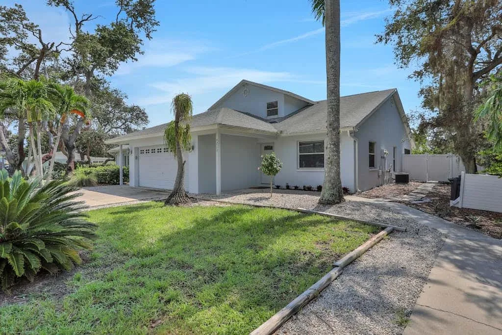 A gray house with a garage stands beside a grassy front yard and driveway.