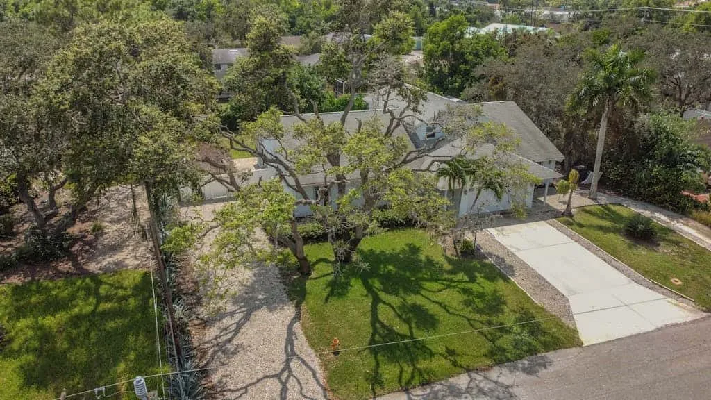 An aerial view of a house with a driveway and a tree-lined yard.