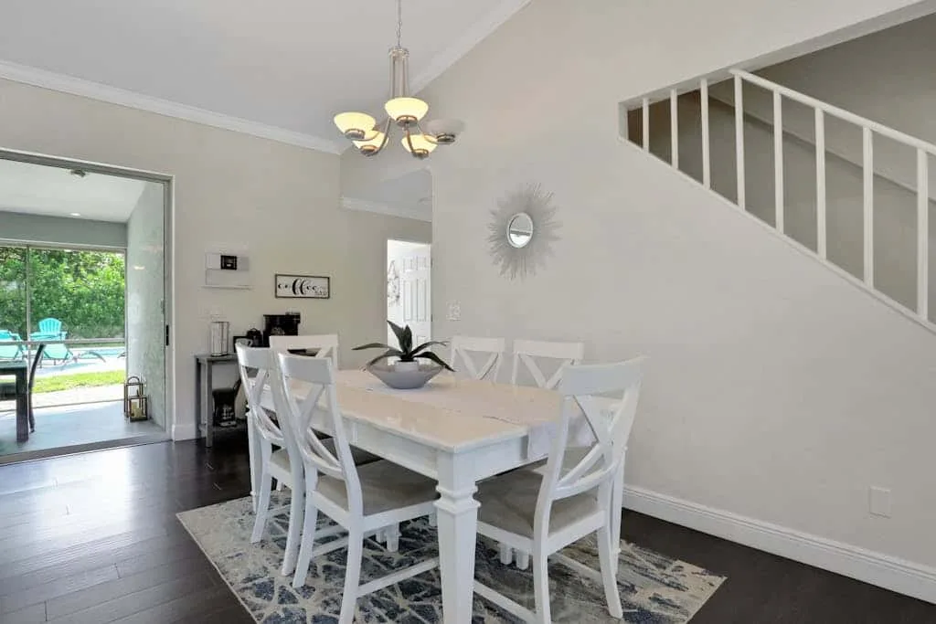 A dining area with a white table and chairs beneath a staircase.