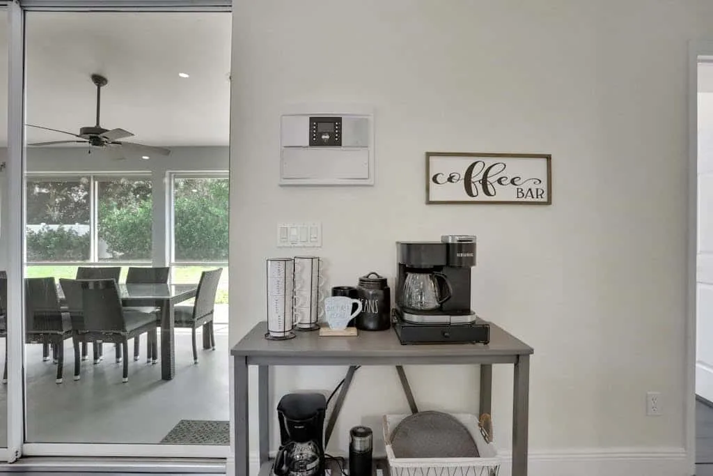 A coffee station stands beside a dining area with a table and chairs.