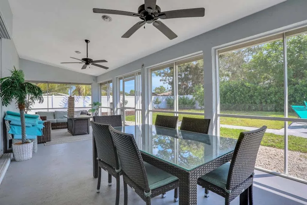 A bright enclosed patio has a glass dining table and large windows overlooking greenery.
