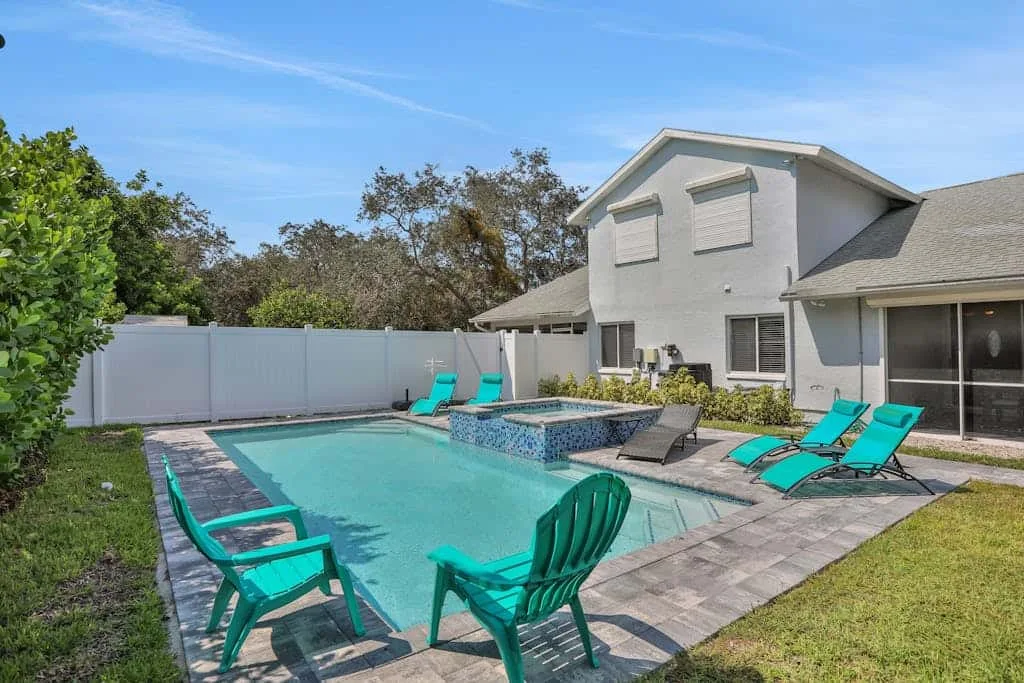 A backyard swimming pool is surrounded by lounge chairs and patio seating.