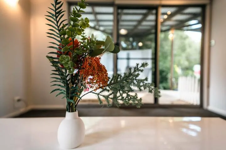 A vase of greenery and orange flowers sits in front of a glass door.