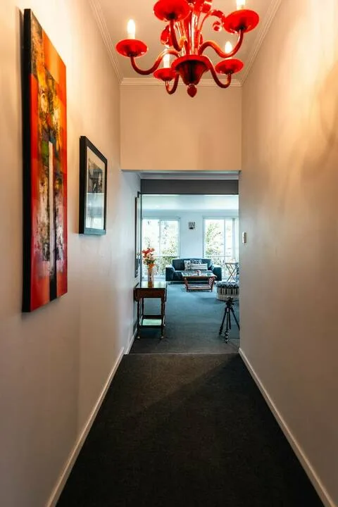 A narrow hallway with wall art leads into a bright sitting area.