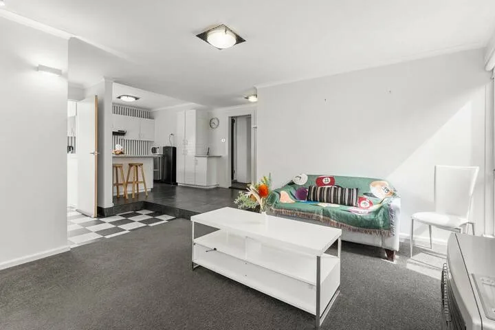 A bright open-plan living room with a kitchenette and a white coffee table.
