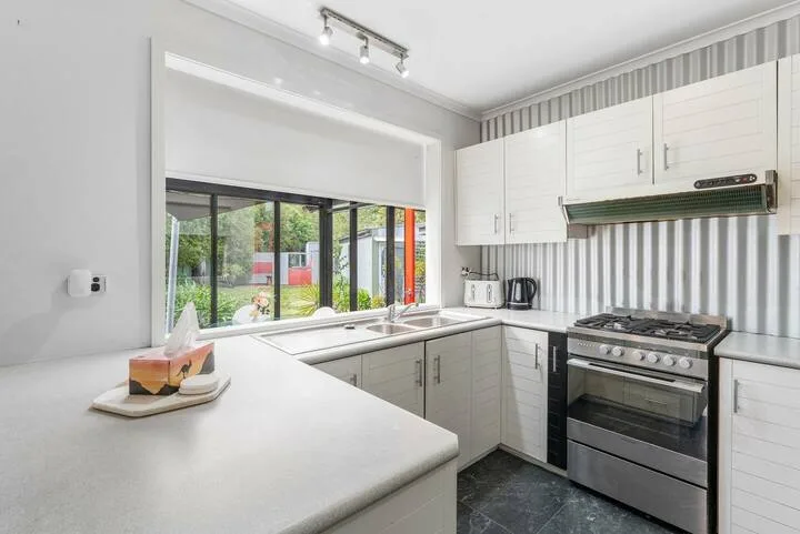 A bright kitchen with white counters, cabinets, and a range beside large windows.