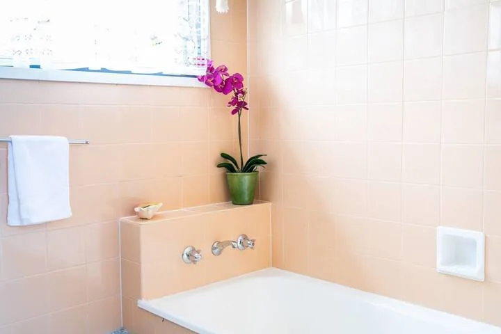 A tiled bathroom with a bathtub, towel, and potted orchid.