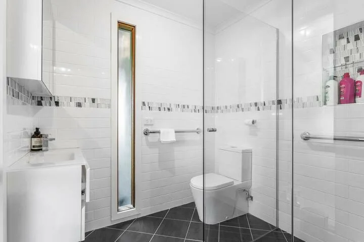 A bright tiled bathroom with a toilet and glass shower panels.