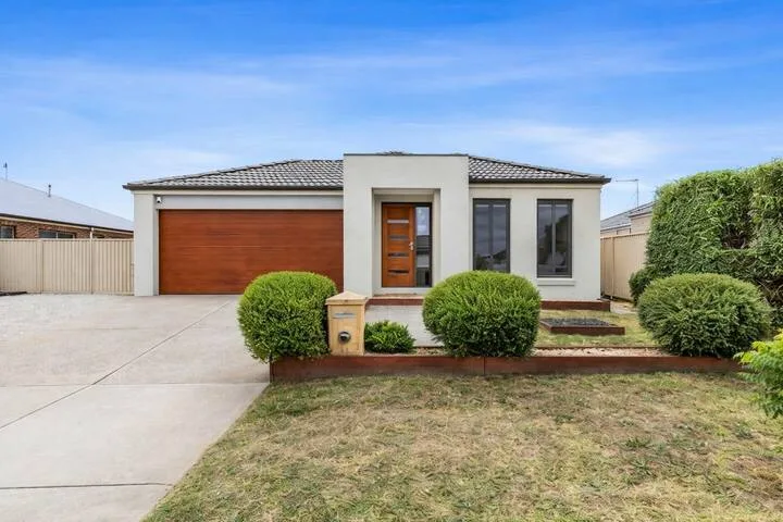 A modern house exterior with a driveway and trimmed shrubs.
