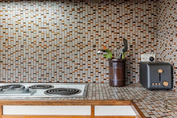 A tiled kitchen counter with a stovetop, utensil holder, and toaster.