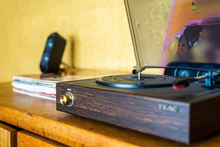 A turntable sits on a wooden table with its transparent dust cover open.
