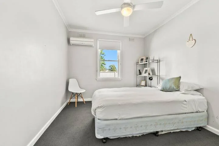 A bright bedroom with a bed, a window, and a small shelving unit.