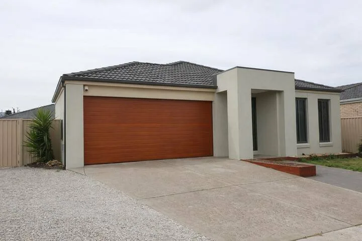 A modern house exterior with a wide wooden garage door and paved driveway.