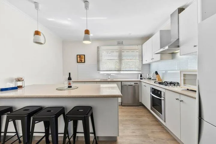 A bright kitchen with a counter, dark seating, and white cabinets.