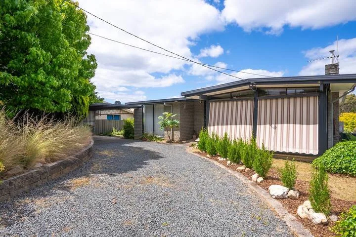 A gravel driveway leads toward a low modern building, bordered by greenery.