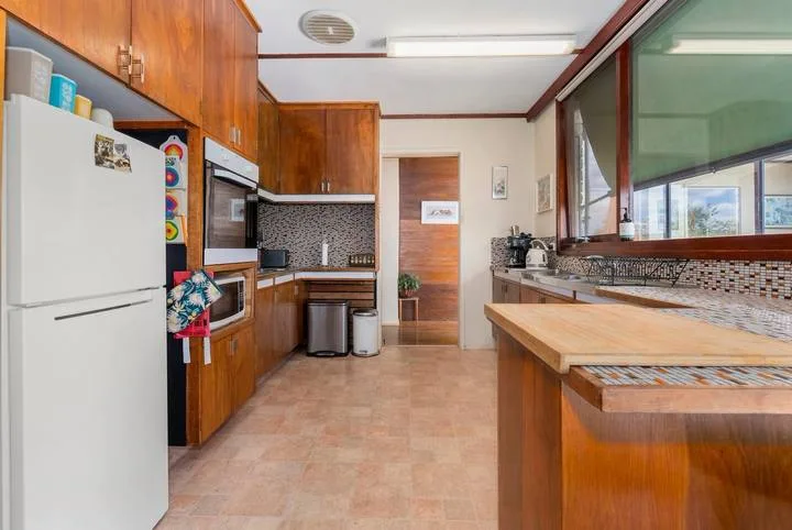 A kitchen with wooden cabinetry, a refrigerator, and a long counter.